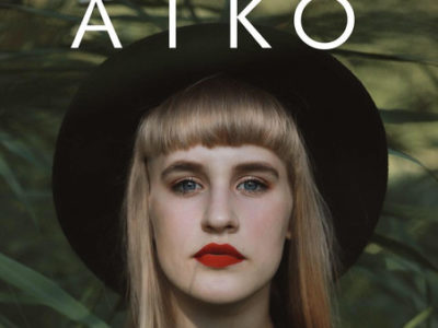 Profil české zpěvačky Aiko v klobouku v zeleném pozadí