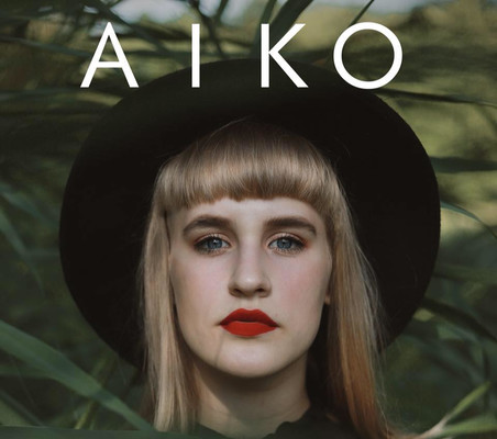 Profil české zpěvačky Aiko v klobouku v zeleném pozadí